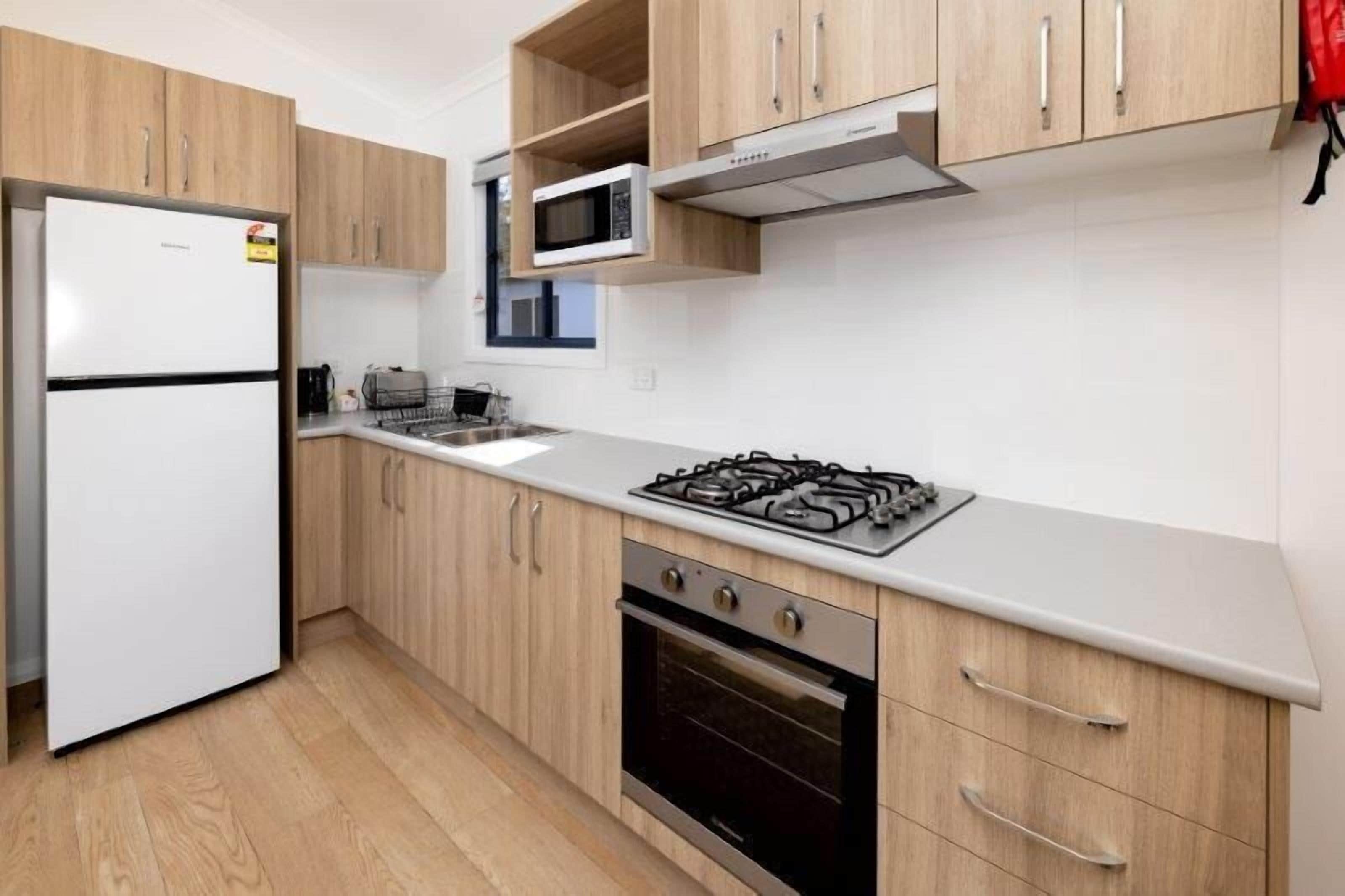 Una cocina moderna con armarios de madera, un refrigerador blanco, un microondas, una estufa a gas y un horno.
