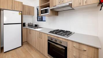 Una cocina moderna con armarios de madera, un refrigerador blanco, un microondas, una estufa a gas y un horno.