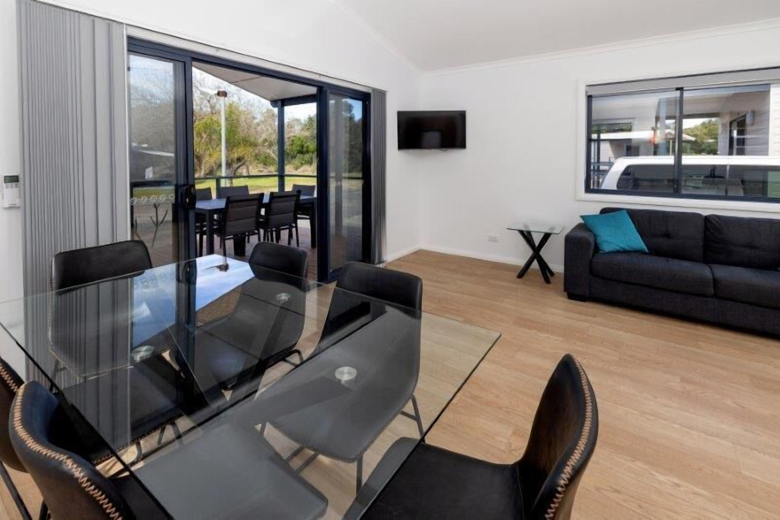 Ein modernes Wohnzimmer mit Glastisch und Stühlen, einer Couch, einem Fernseher und einem Balkon mit Sitzgelegenheit.