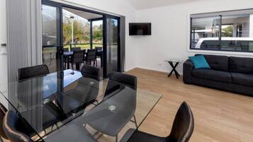 Ein modernes Wohnzimmer mit Glastisch und Stühlen, einer Couch, einem Fernseher und einem Balkon mit Sitzgelegenheit.