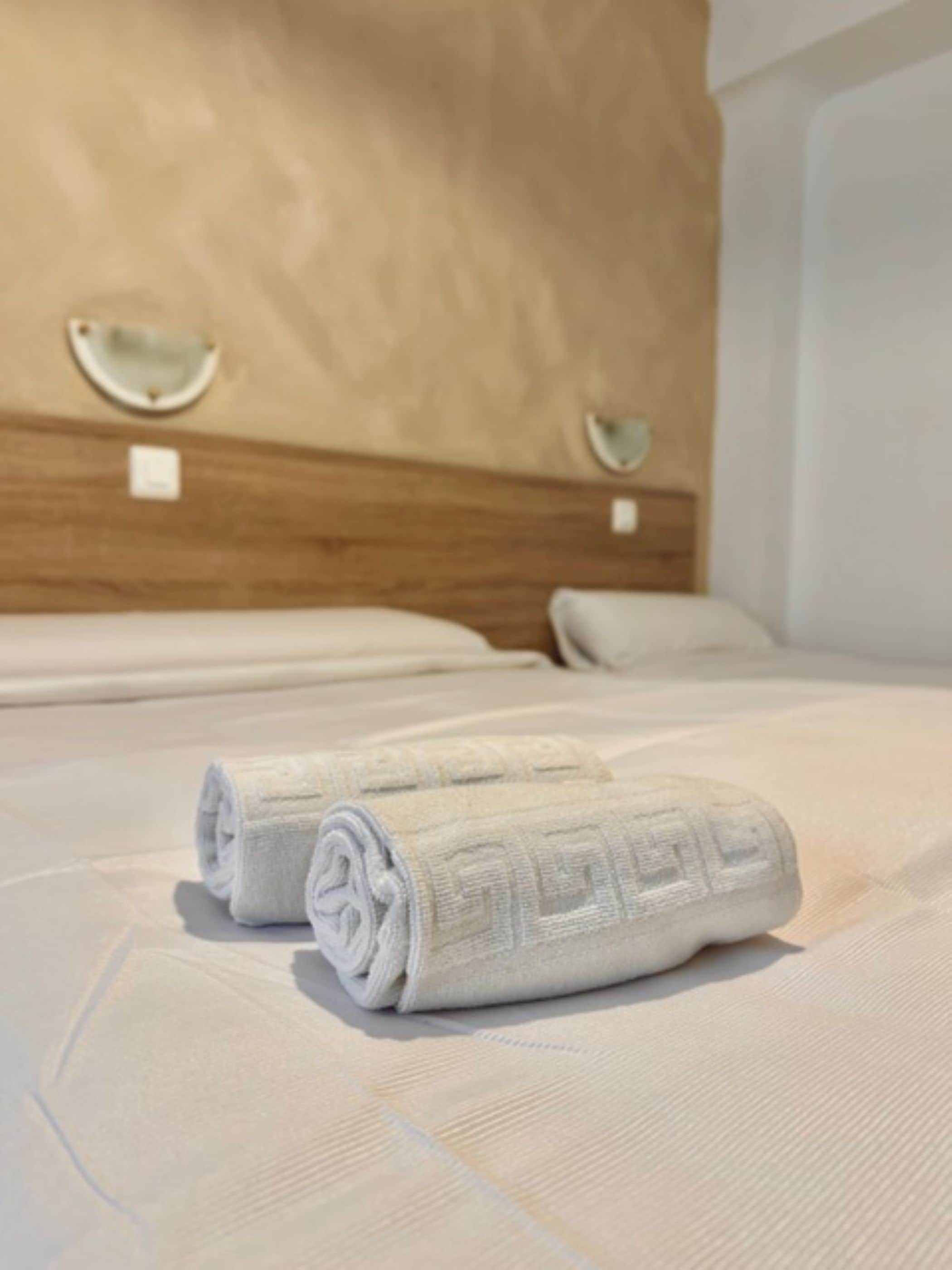 Una cama bien hecha con dos toallas enrolladas y un cabecero de madera.