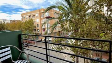 A balcony with metal chairs, a view of a building, and a palm tree.