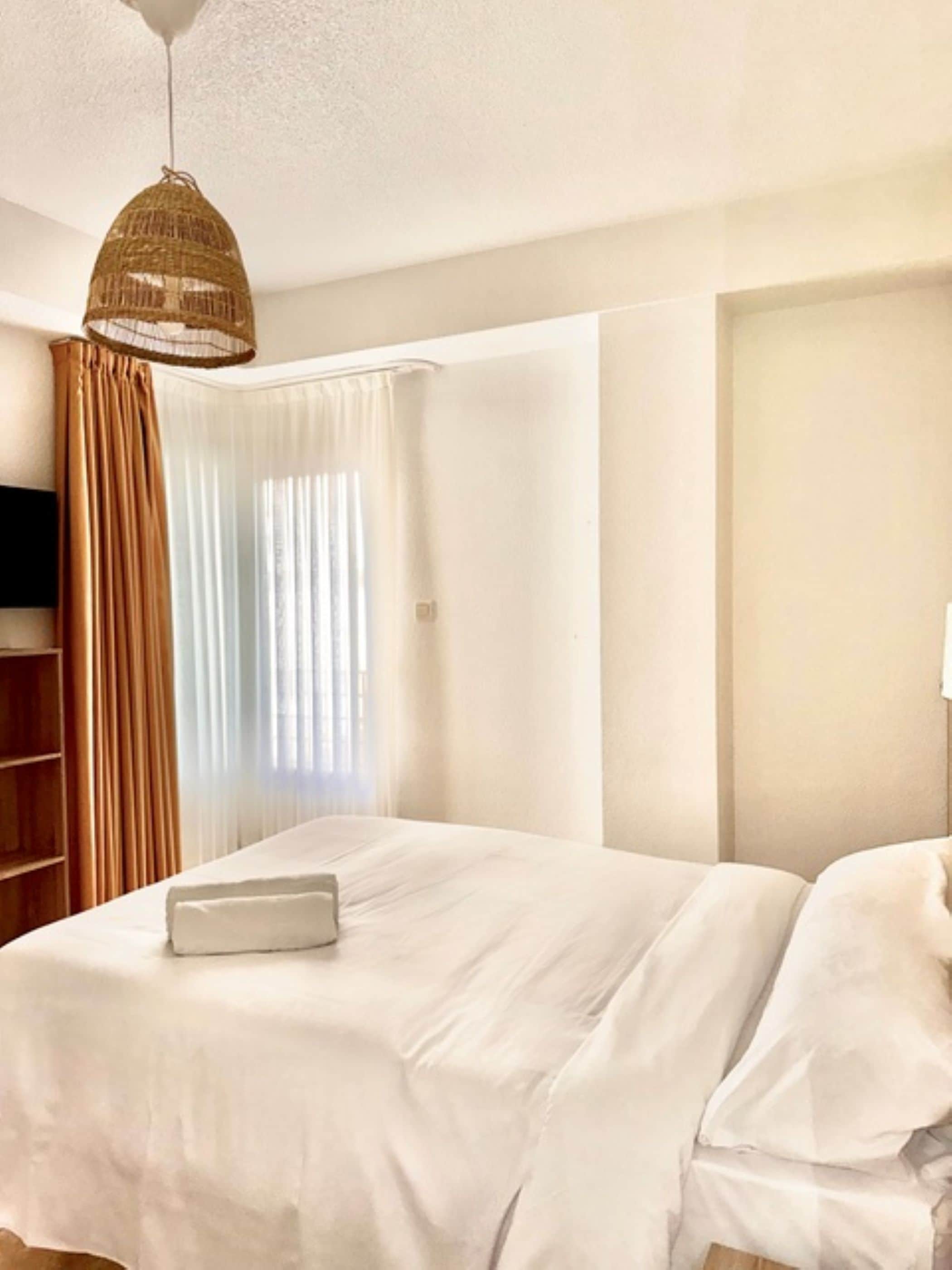 A hotel room with a bed, curtains, a television, and a hanging light fixture.