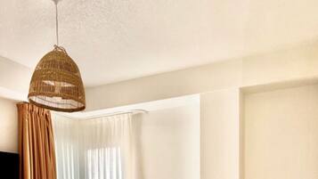 A hotel room with a bed, curtains, a television, and a hanging light fixture.