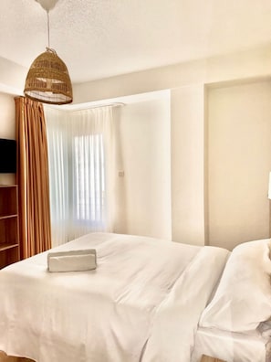 A hotel room with a bed, curtains, a television, and a hanging light fixture. - HS Altet Suites (Elche)