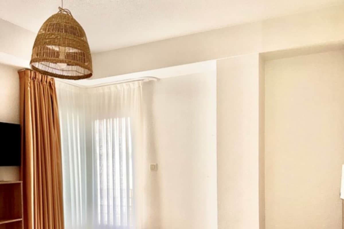 A hotel room with a bed, curtains, a television, and a hanging light fixture.