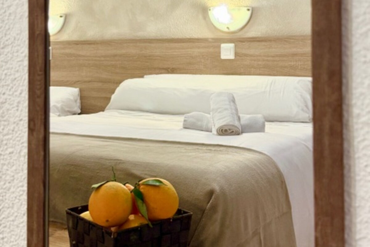 Una habitación de hotel con una cama, una mesita de noche con una cesta de frutas y luces fijadas a la pared.