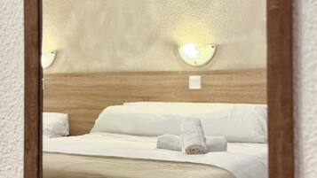 A hotel room with a bed, a nightstand with a fruit basket, and wall-mounted lights.