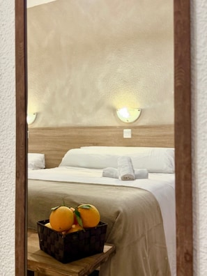Una habitación de hotel con una cama, una mesita de noche con una cesta de frutas y luces fijadas a la pared.