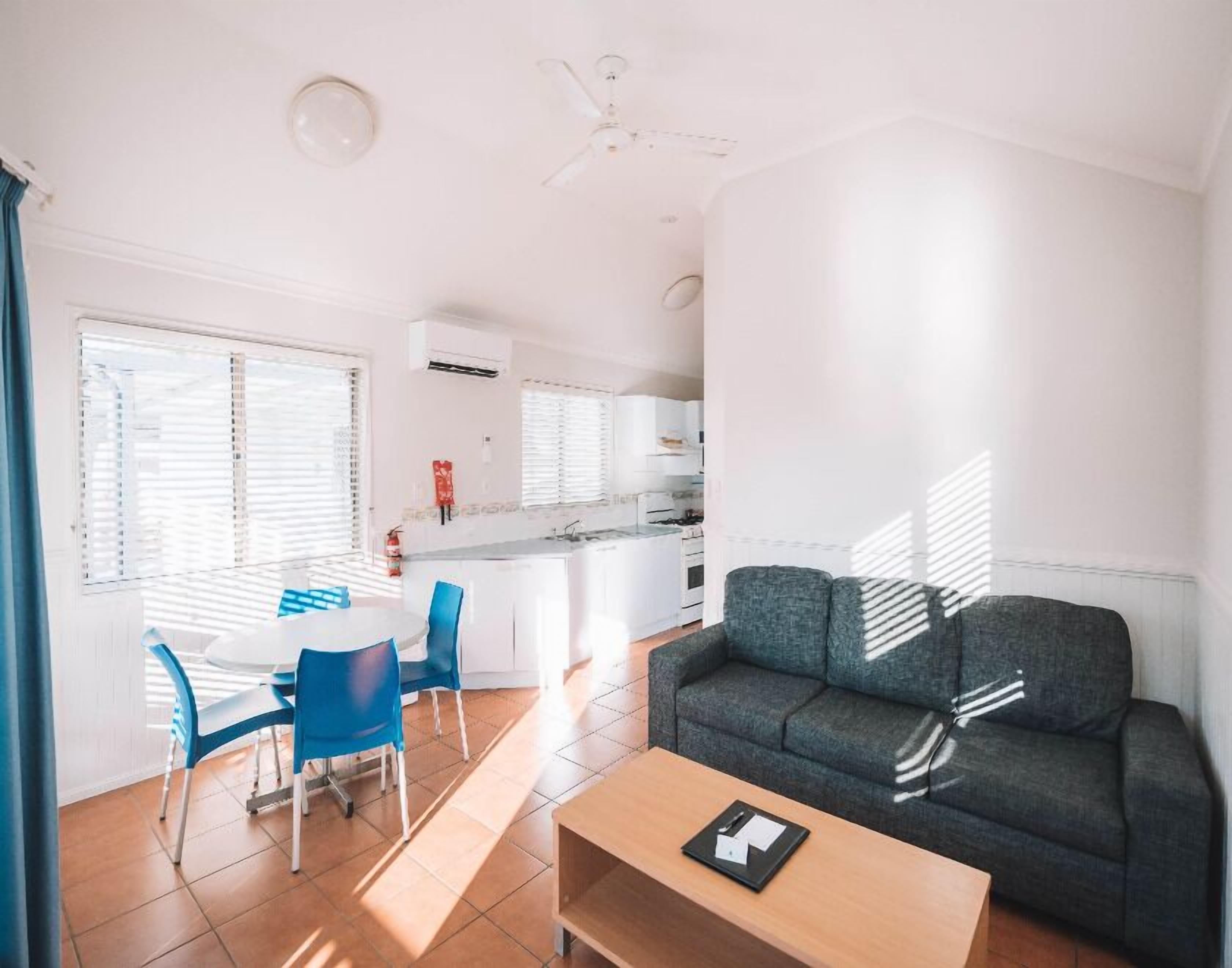 A modern living room with a sofa, a dining table with chairs, a kitchen area, and a ceiling fan.