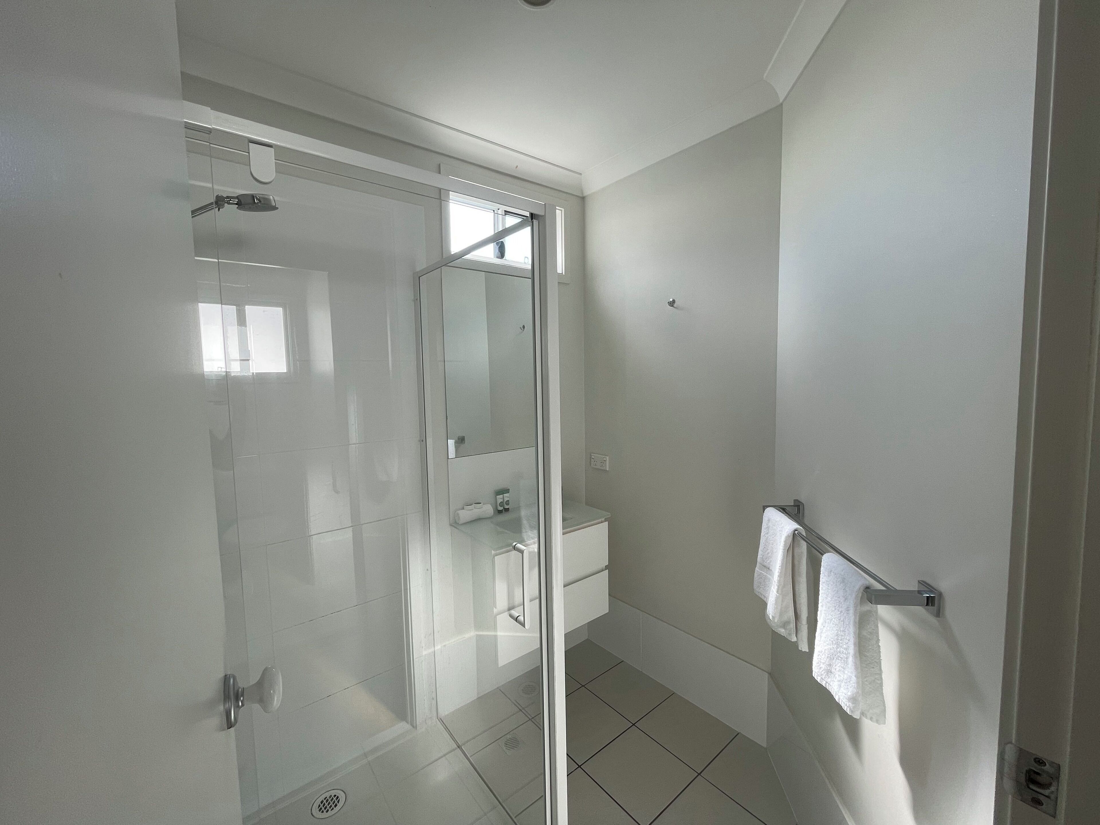 A modern bathroom with a glass shower enclosure, a white sink, and a towel rack.