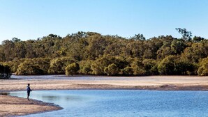 A person fishing by a calm river with dense forest in the background. - BIG4 Rainbow Beach Holiday Park (Rainbow Beach)