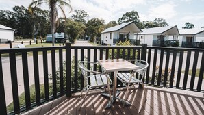 A deck with a table and chairs, overlooking a street with mobile homes and a palm tree. - BIG4 Rainbow Beach Holiday Park (Rainbow Beach)
