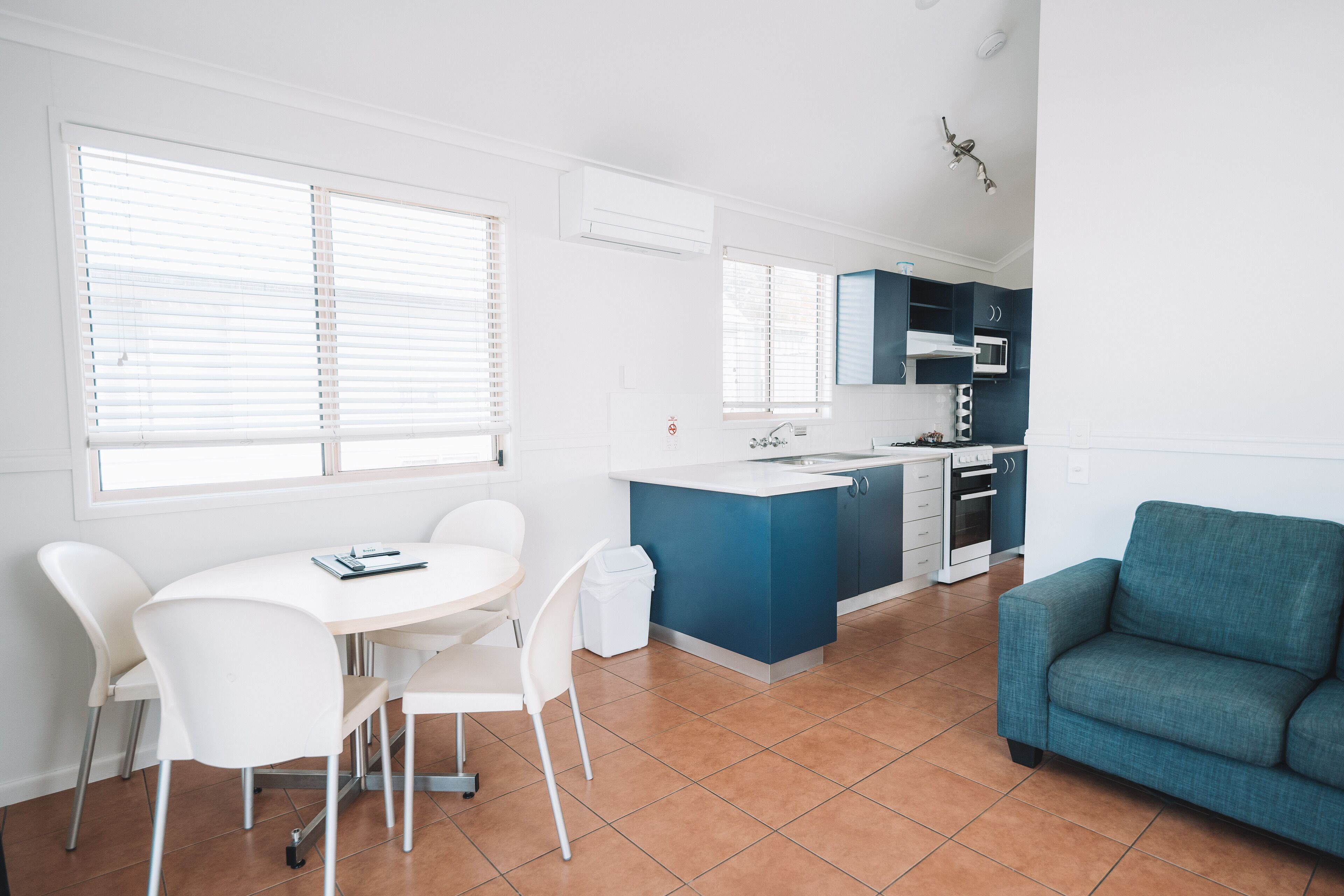 A modern kitchen with white and blue cabinets, a white dining table with chairs, and a teal sofa.
