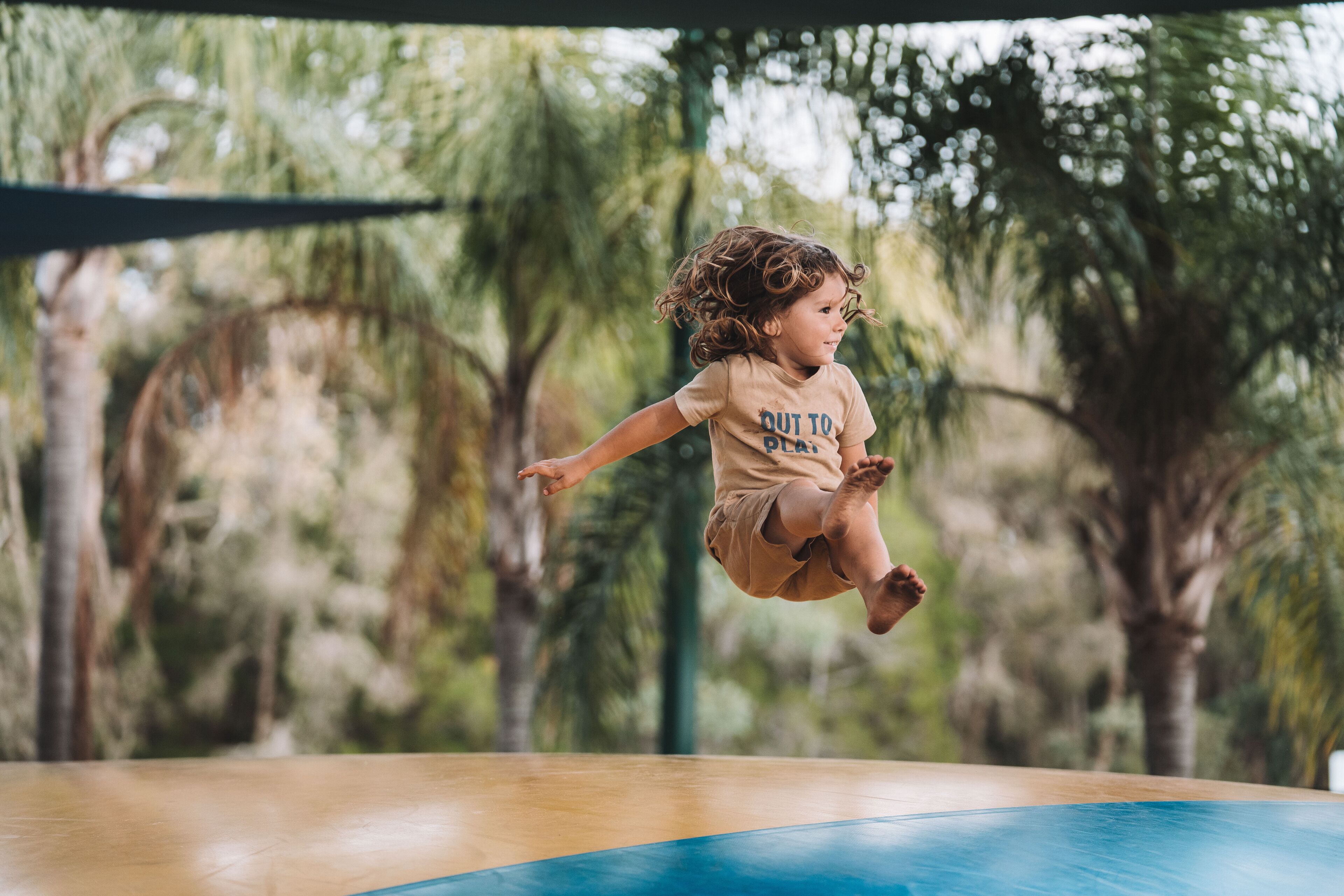 A child jumping on a trampoline with a blurred outdoor background.