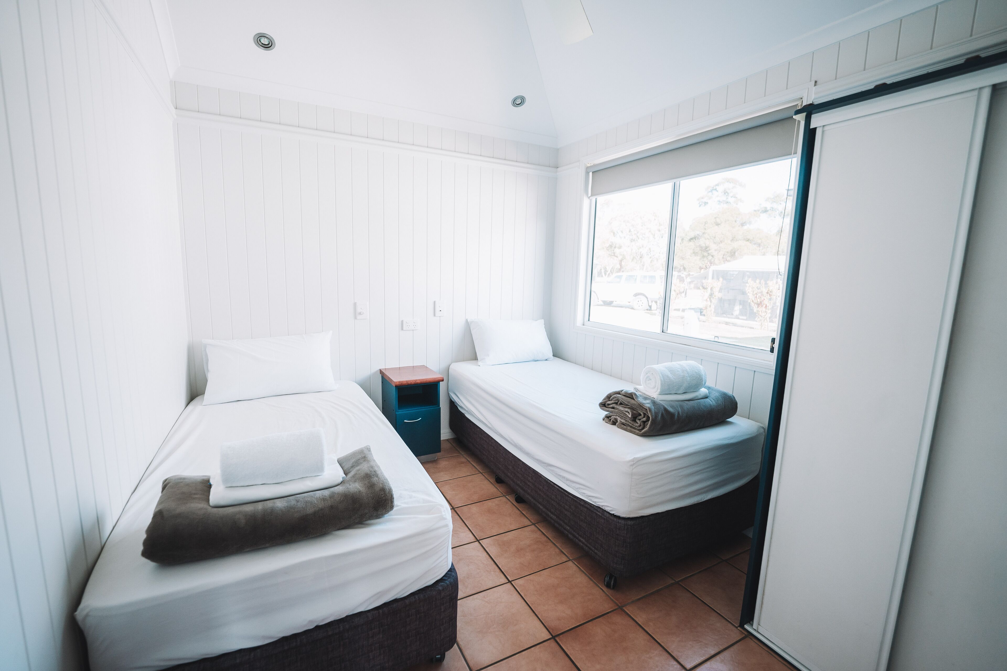 Une petite chambre propre, avec deux lits simples, une fenêtre et une porte coulissante.
