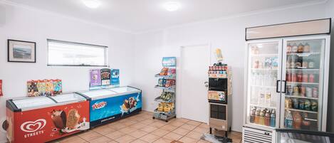 A clean, well-lit convenience store with a freezer section, snack shelves, and a refrigerated beverage display.