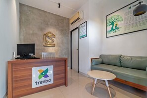 A reception area with a wooden desk, a green sofa, and a small round table. - Treebo Corner Stay, Coimbatore (Coimbatore)
