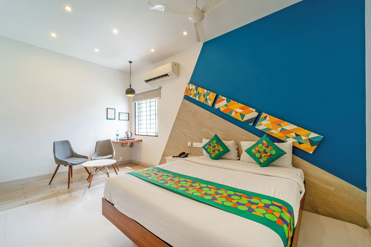 A modern hotel room with a bed, two chairs, a desk, and a window.