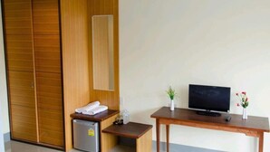 Una habitación compacta con un armario de madera, un refrigerador pequeño, una mesa de madera con un televisor y una planta en maceta.