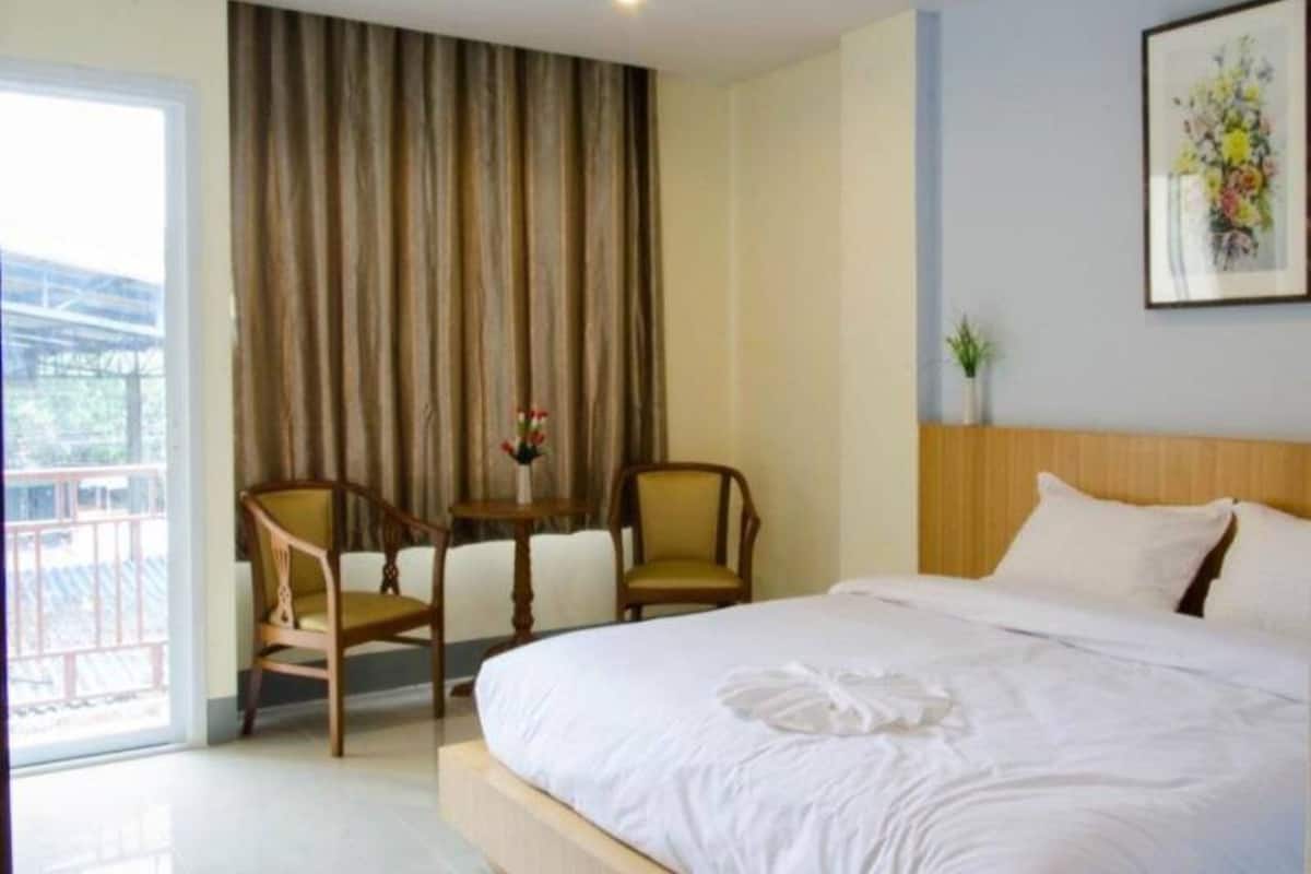 A hotel room with a bed, two chairs, a small table, a curtain, and a framed picture on the wall.