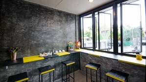 Zona de bar con una decoración en tonos negro y amarillo, una ventana con vistas al exterior y una estantería con diversos objetos.