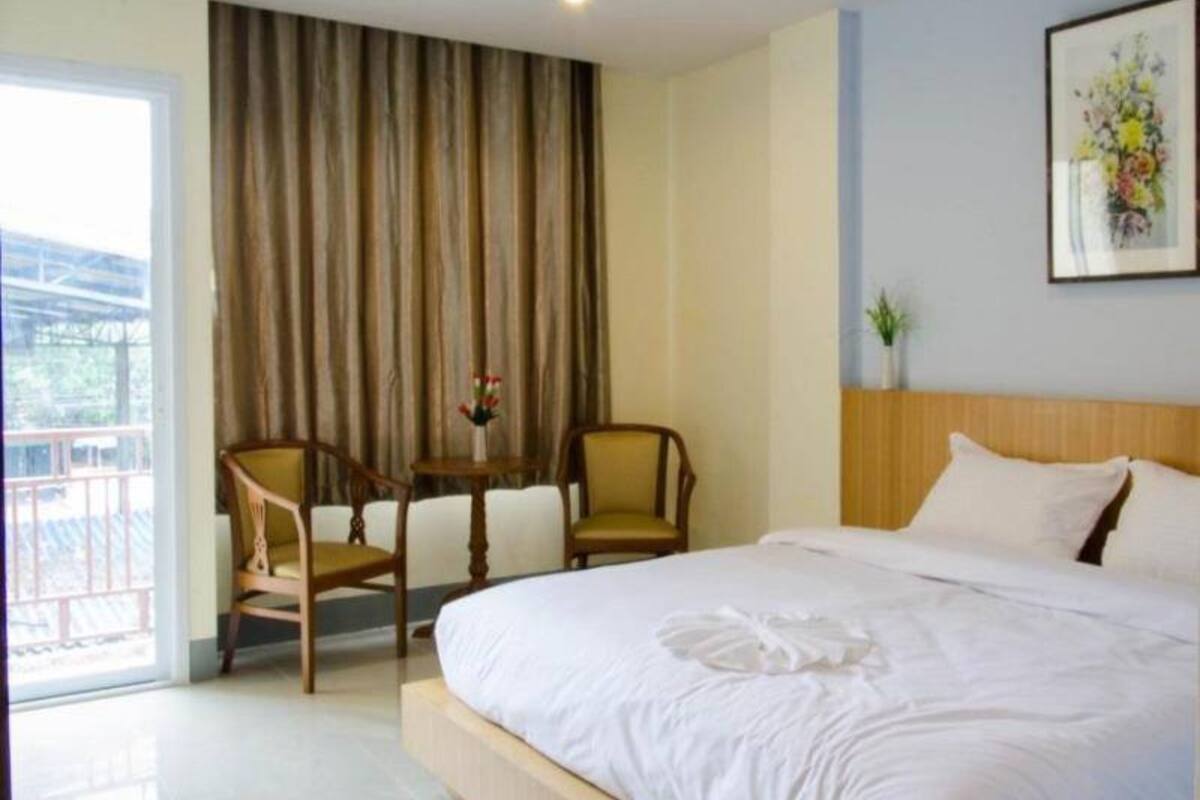 A hotel room with a large bed, two chairs, a small table with flowers, and a view of the outdoors.