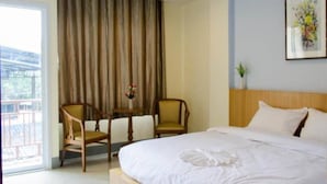 Habitación de hotel con una cama grande, dos sillas, una mesita con flores y vistas al exterior.