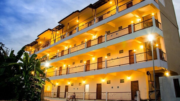 Un hotel de varios pisos con balcones, iluminación cálida y un paisaje tropical.