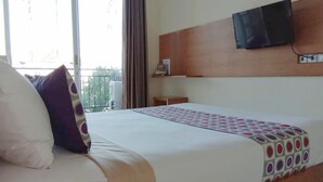 A hotel room with a bed, a TV mounted on the wall, a window with curtains, and a balcony view. - Hotel Mandari (Buleleng)