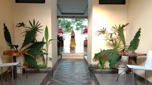 A corridor with a tiled floor leading to a balcony. There are potted plants on either side and a statue in the center. - Hotel Mandari (Buleleng)