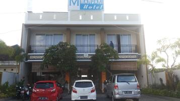 Hotel con letrero, entrada cubierta y zona de estacionamiento con coches.