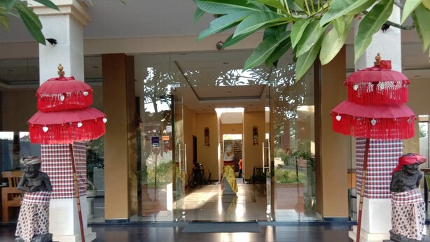 A hotel entrance with a glass door, red umbrellas, and statues on pedestals. - Hotel Mandari (Buleleng)