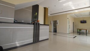 A modern reception area with a glass partition, a reception desk, and a seating area with chairs and a table. - Hotel Mandari (Buleleng)