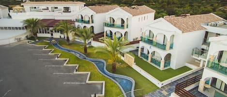 A modern hotel with multiple balconies, a swimming pool, and a landscaped garden.