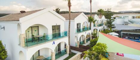 A white building with balconies, a pool, and palm trees.