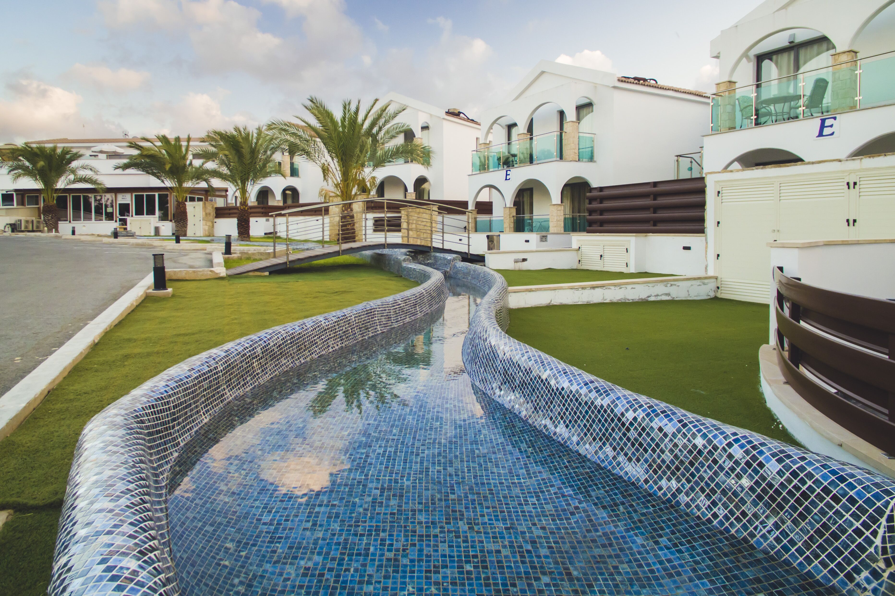 A swimming pool with mosaic tiles, surrounded by a well-maintained lawn and palm trees.