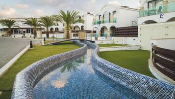 A swimming pool with mosaic tiles, surrounded by a well-maintained lawn and palm trees.