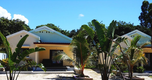 Una hilera de edificios de dos pisos con techo plano, rodeados de vegetación tropical.