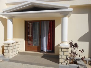 A building entrance with a wooden door, white columns, and a small potted plant.