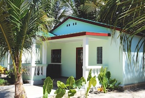 A single-story house with a light blue exterior and a red roof, surrounded by lush greenery.
