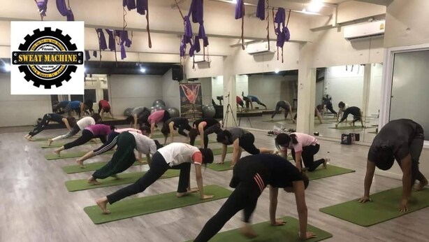 Un cours de yoga dans un studio aux murs recouverts de miroirs et doté de tapis verts.