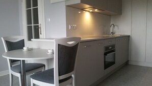 A modern kitchen with a round dining table and two chairs, a built-in oven, and a stainless steel sink. - Old Town Art Apartment (Warsaw)