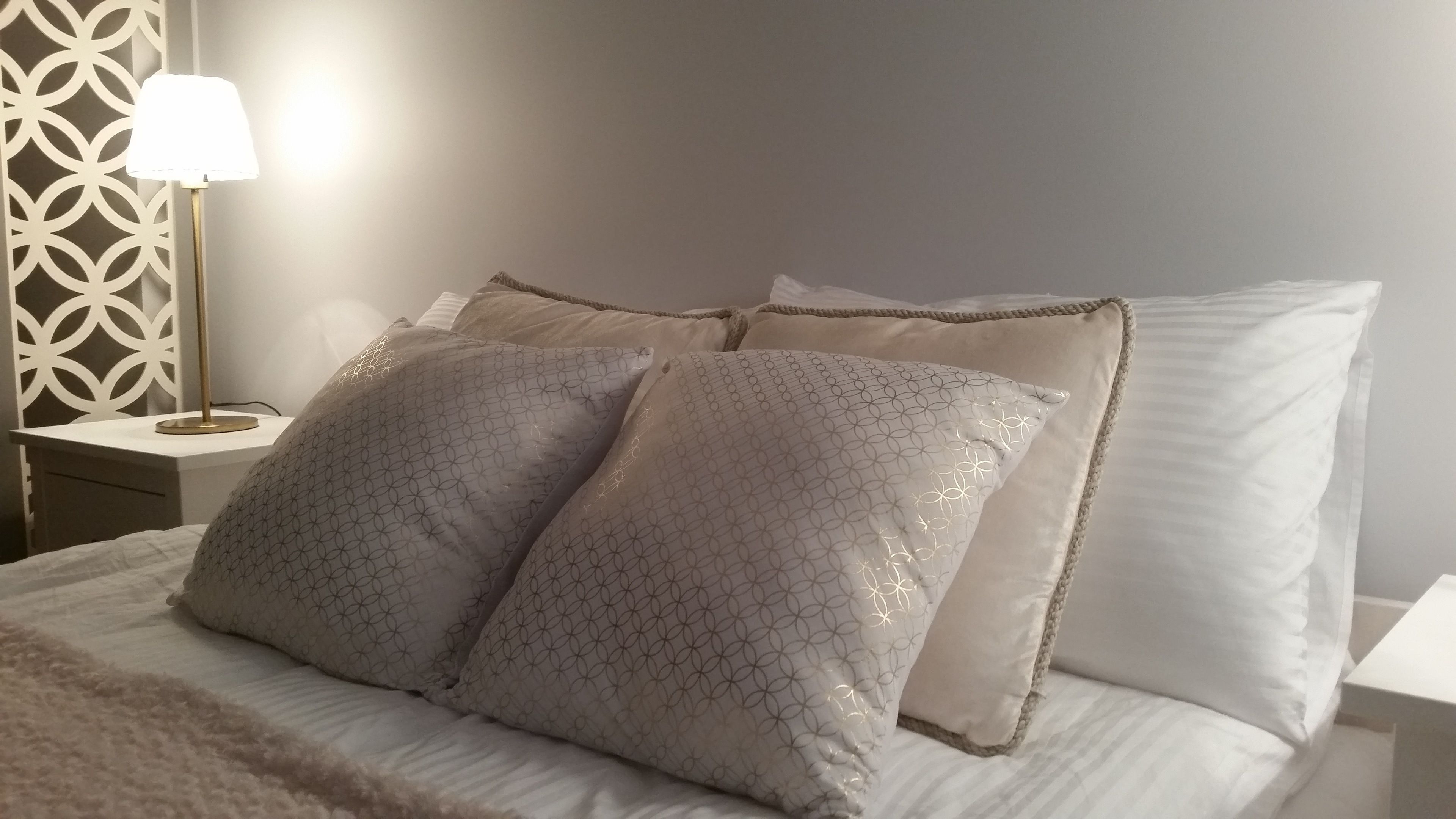 Un lit bien fait, agrémenté d’oreillers à motifs et d’une lampe de chevet.