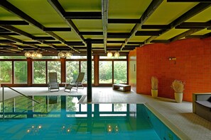 A swimming pool with a glass floor, wooden ceiling beams, and large windows offering a view of greenery. - Hotel Orbtal (Bad Orb)