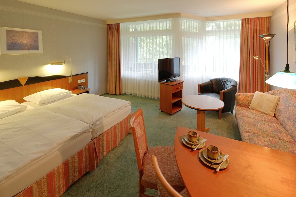 A hotel room with a bed, a sofa, a small table with a cup and saucer, a television, and a lamp.