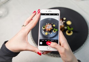 A person holding a smartphone with a food photo displayed on the screen. - Historic Hotel La Stua (Cavalese)