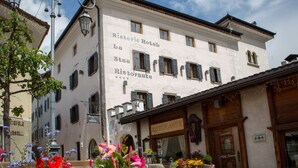 A historic hotel with a restaurant on the ground floor, featuring a stone facade and a cobblestone street in front. - Historic Hotel La Stua (Cavalese)