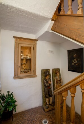 A staircase with wooden balusters, a wooden cabinet with glass doors, and two wooden sculptures on the wall. - Historic Hotel La Stua (Cavalese)