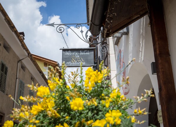 A narrow street with a sign for "histo hotel la scua reectorum" and a building with a mural. - Historic Hotel La Stua (Cavalese)